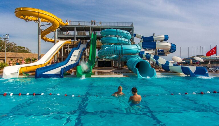 Two guests swim in a blue pool in front of spiral and open water slides