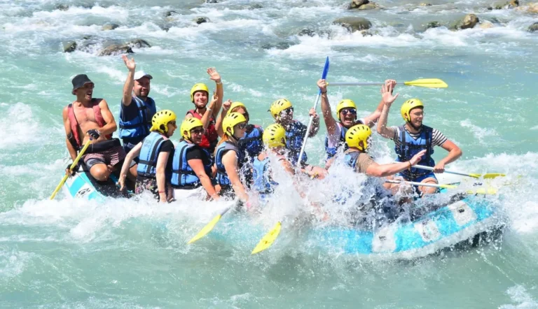 Guests in yellow helmets raise paddles and hands on a raft in Köprülü Canyon