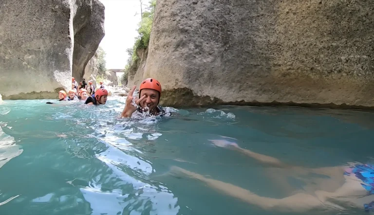 Guests in helmets swim between pale rock walls in Köprülü Canyon, one waving at the camera