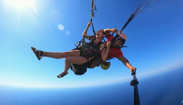 A smiling guest and pilot glide in a tandem harness over the open blue sea