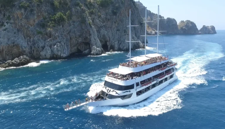 Crowded boat turns past rocky cliffs and sea caves on turquoise water