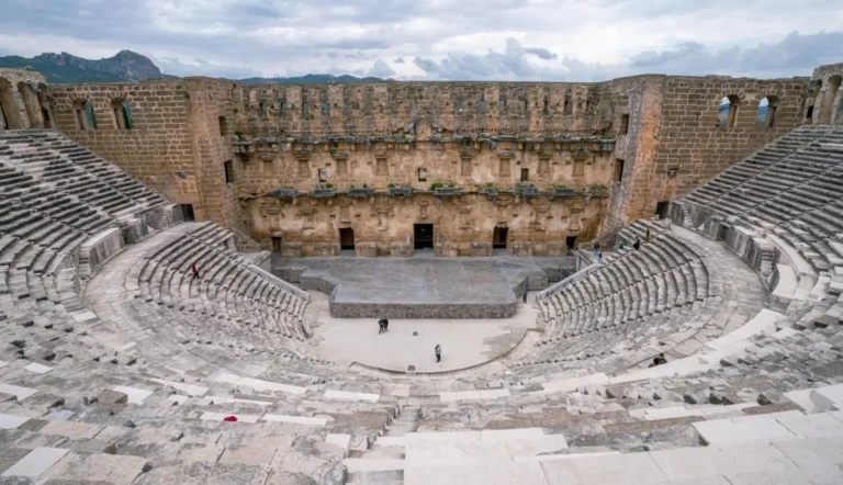 Stone seating rows and stage building inside the Roman theatre of Aspendos under cloudy sky