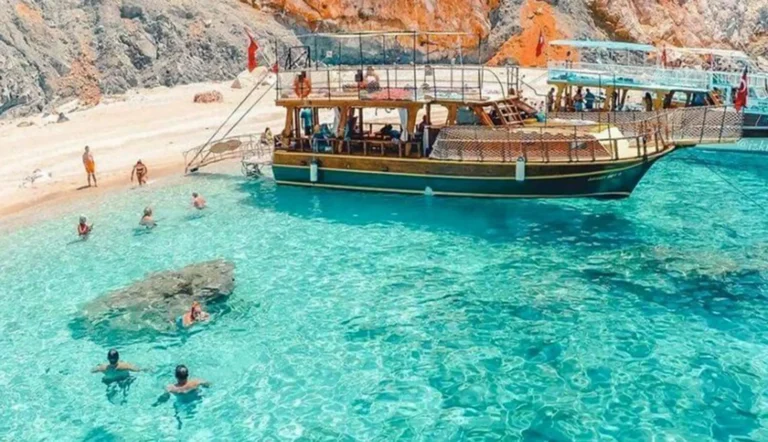 Guests swim in clear turquoise water beside a moored wooden boat at Suluada beach