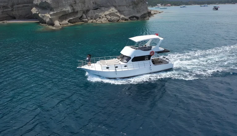 White motor yacht with a flybridge passing pale rocky cliffs on turquoise water